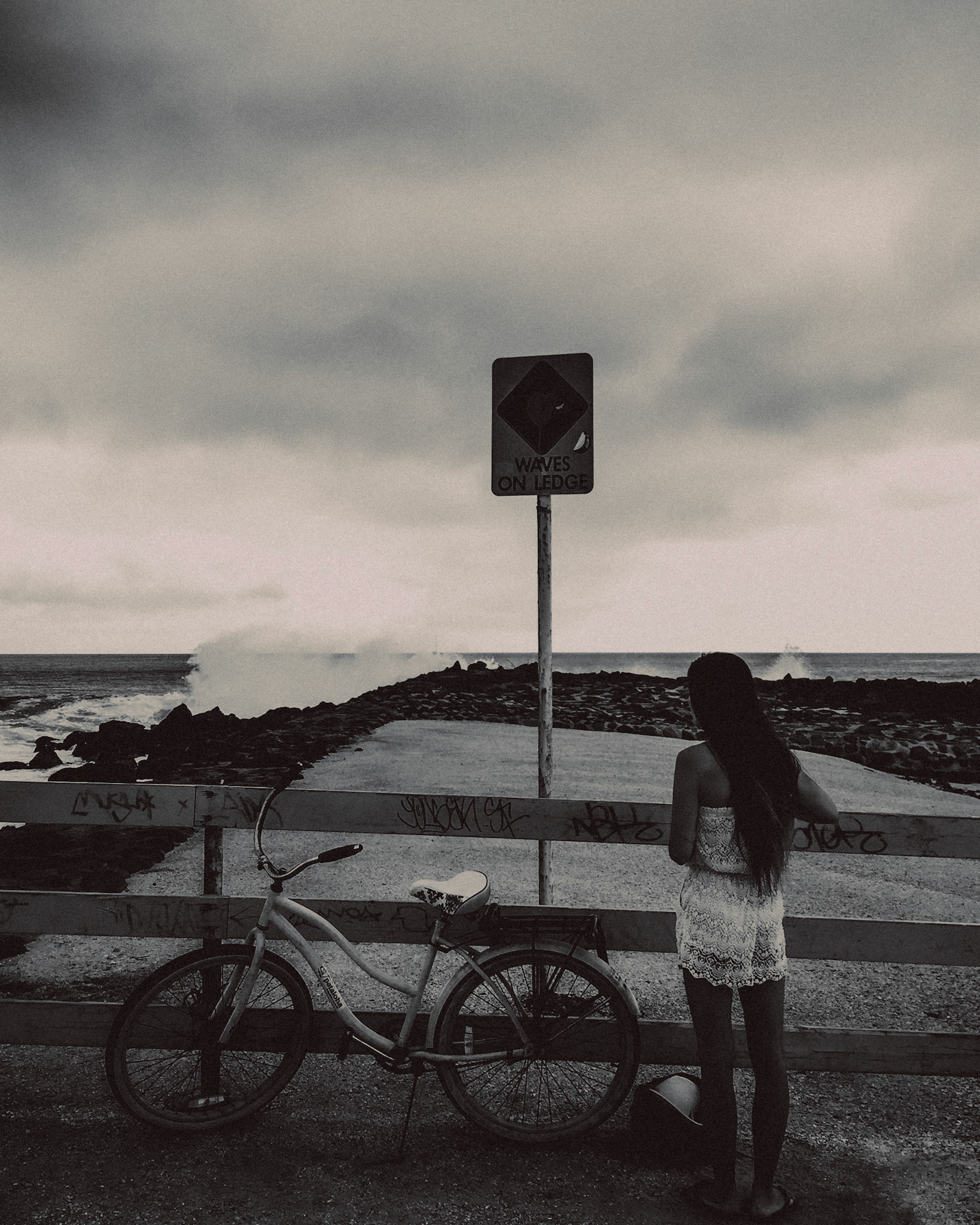 A woman and her bike on a breakwater in Waikiki Beach, in black and white, Honolulu, Hawaii, USA, September 2015, iPhone 6 Plus.