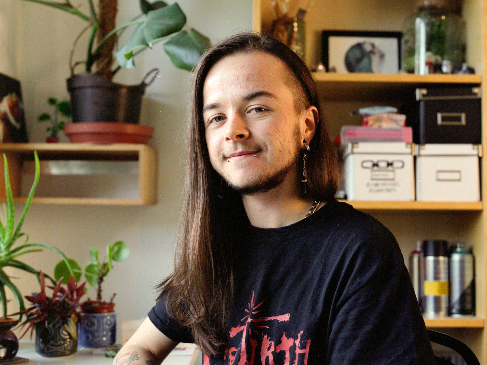 Leo is sitting at his desk and smiling into the camera. There are various plants around him in the background.