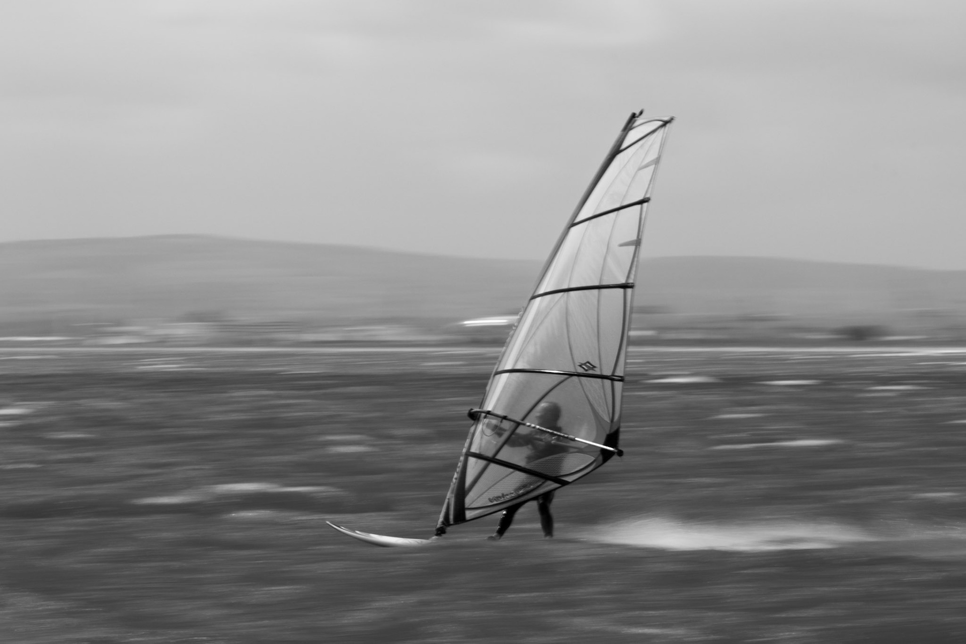 Black and white shot of a windsurfer in Dublin Bay.  Motion blur accentuated using slow panning with slow shutter speed.
