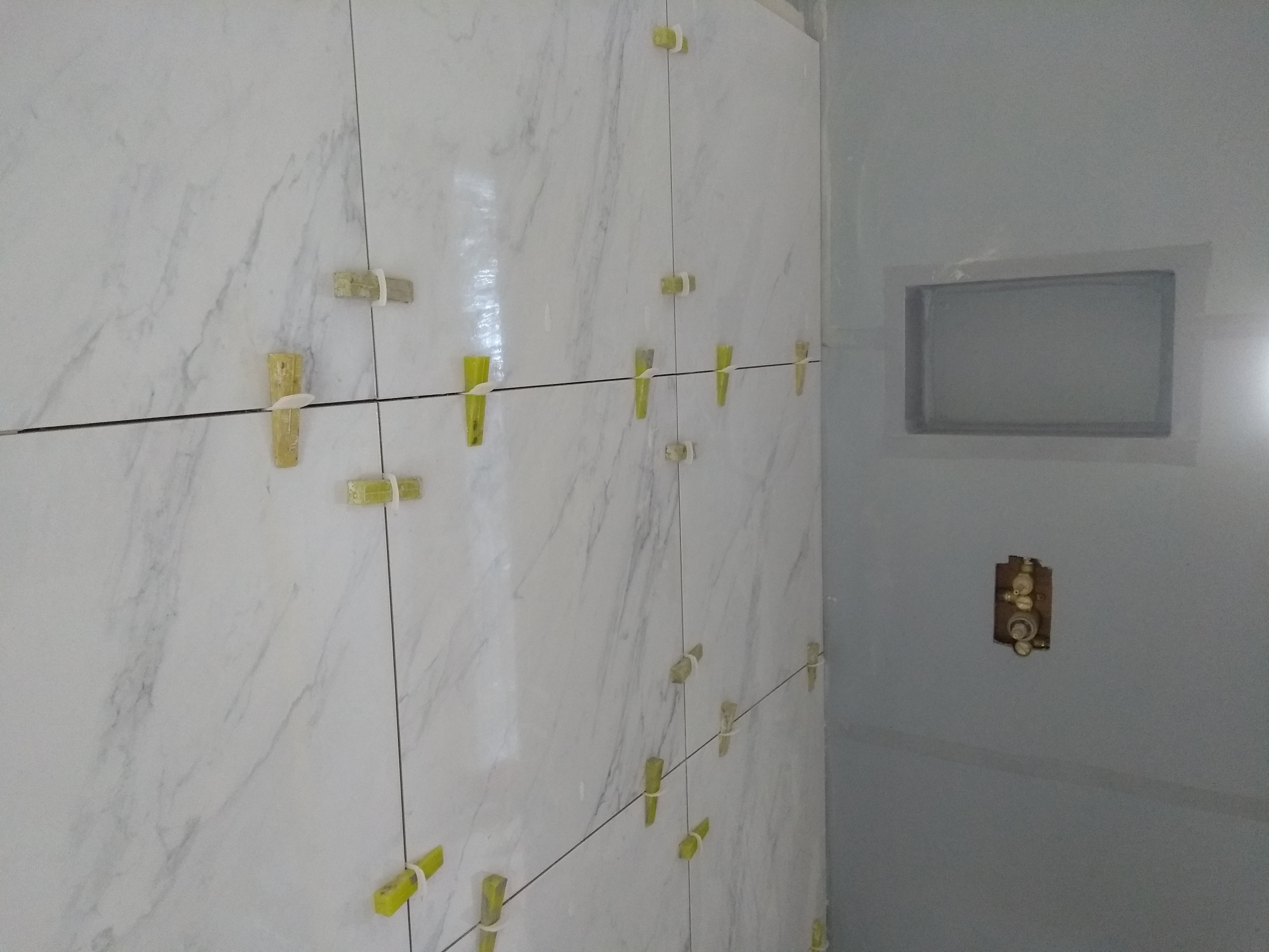 Tiles being installed using a leveling system to a tanked shower area with a 'niche'