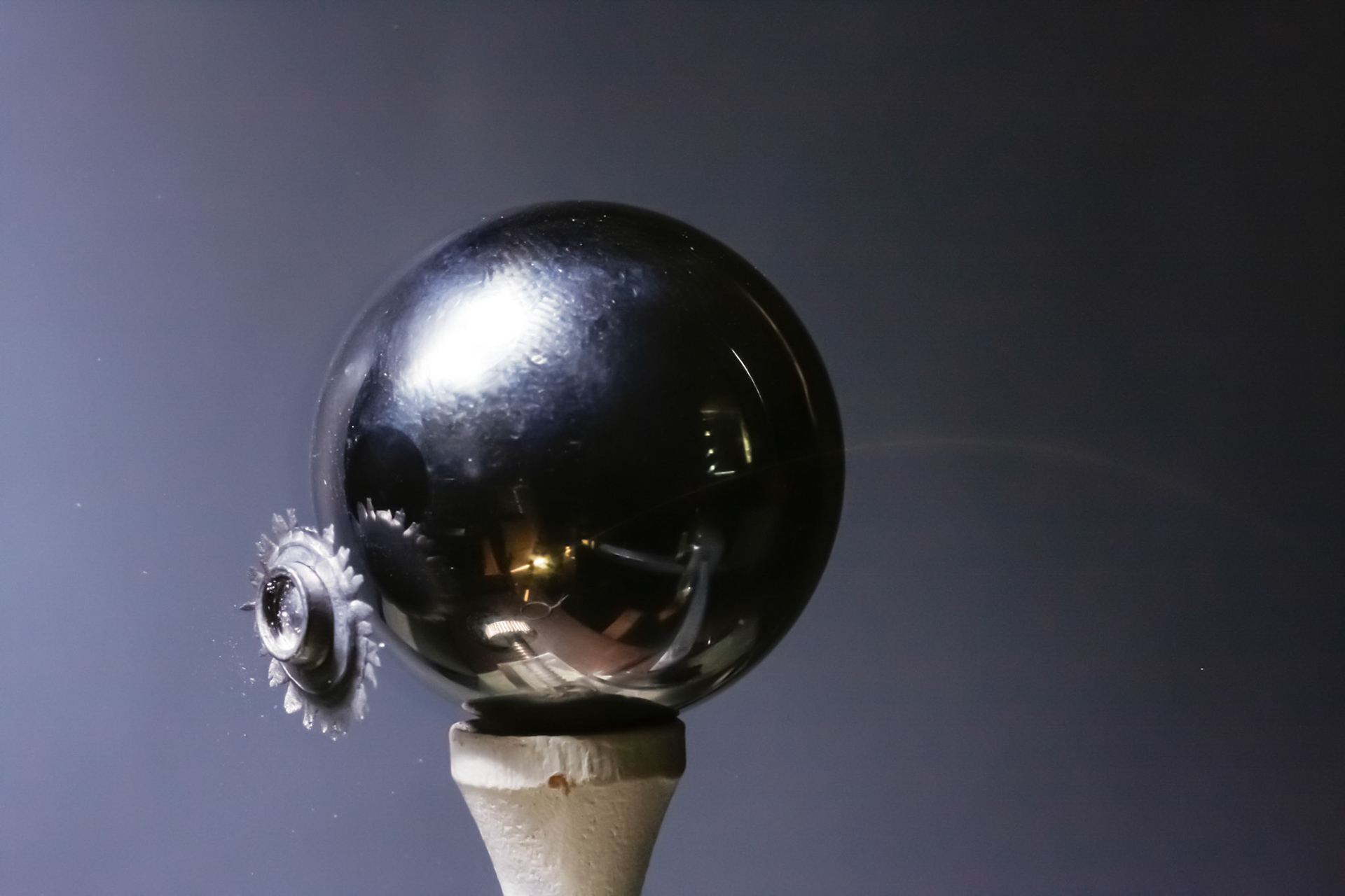 Air pellet rebounding from steel ball on golf tee. The arc in front of the ball is the trajectory of the specular highlight