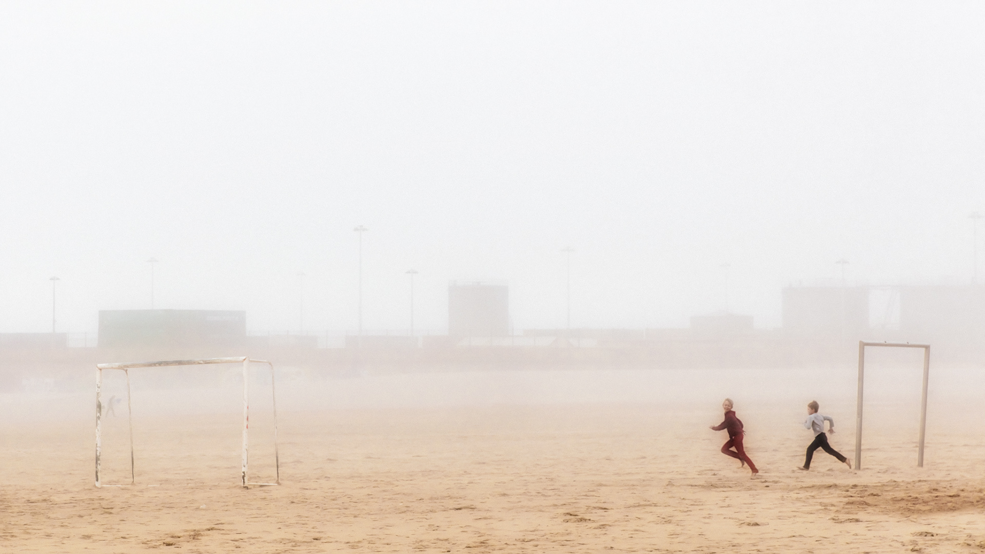 Fine art photography: children running int he beach soccer field around fog.