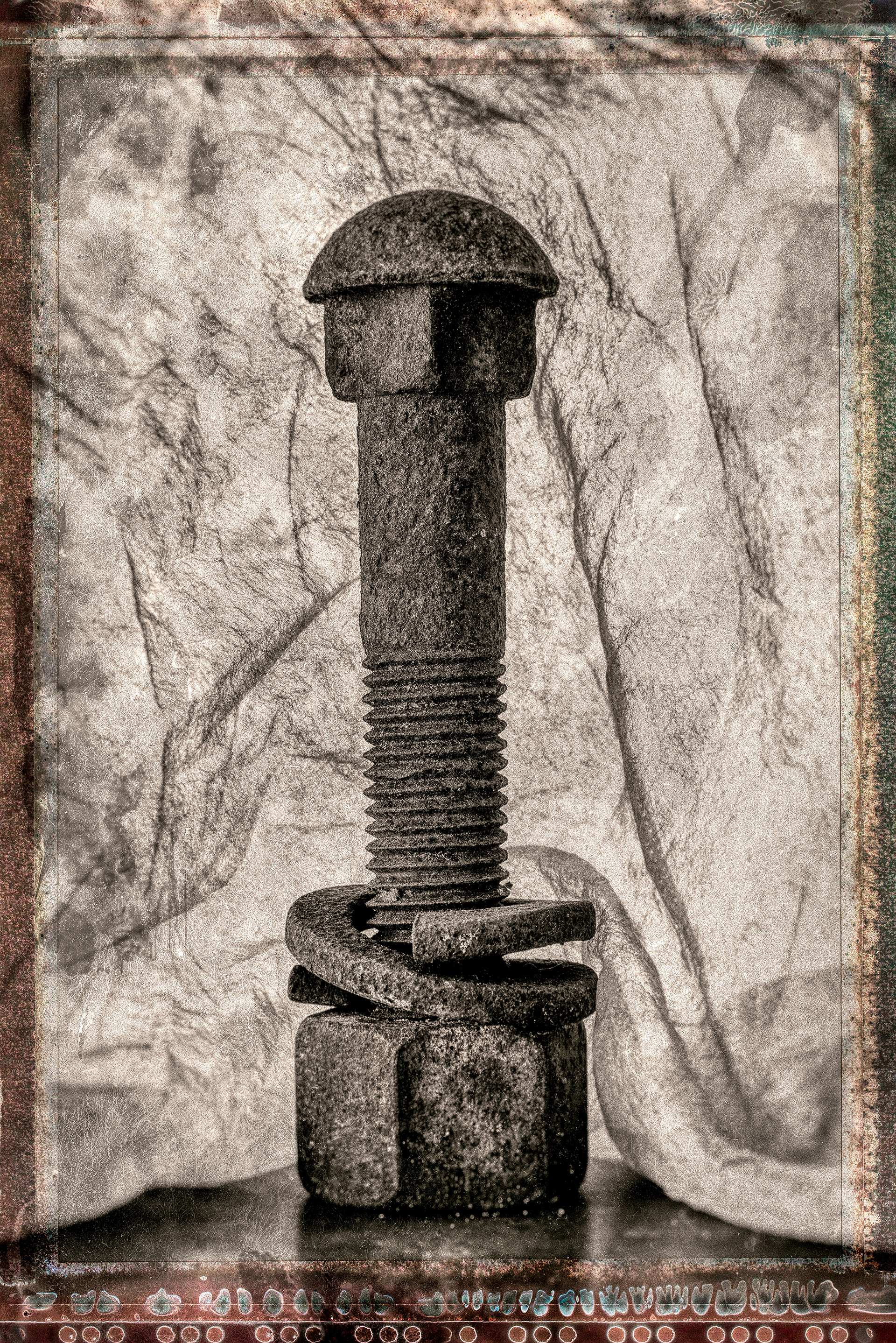 A large nut and bolton a hard suface draped with a light cloth. Photographed with a distressed look,sepia toned and with a large format polaroid type border