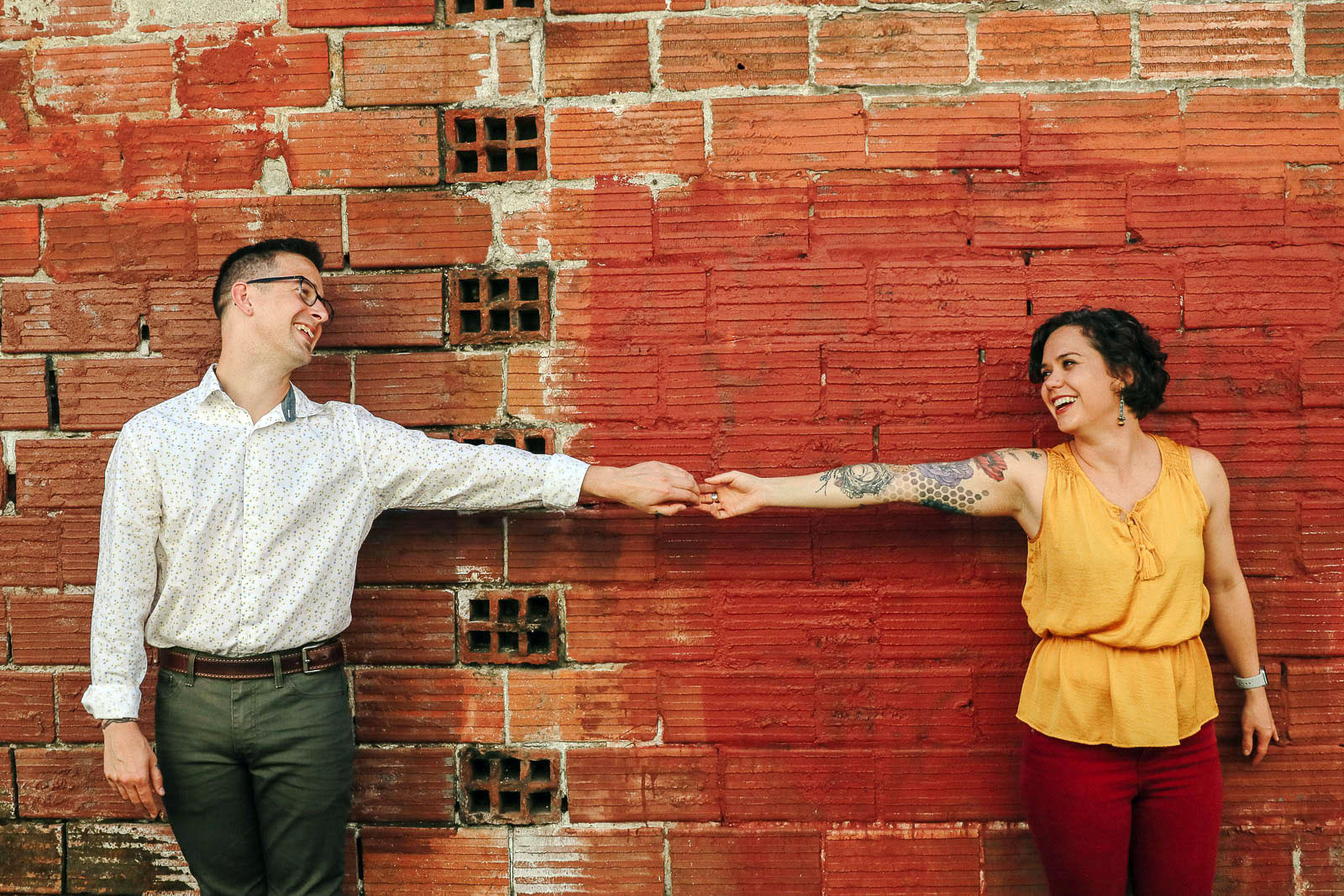 Young couple engaged to by married, holding hands in front of red brick wall