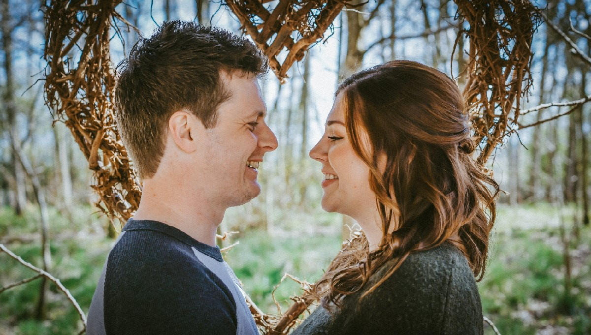photo taken by photographer david lefebvre from buckinghamshire at new woodland wedding venue called endeavour the happy couple are stood smiling at each other with a blue sky and wooden woven heart behind them