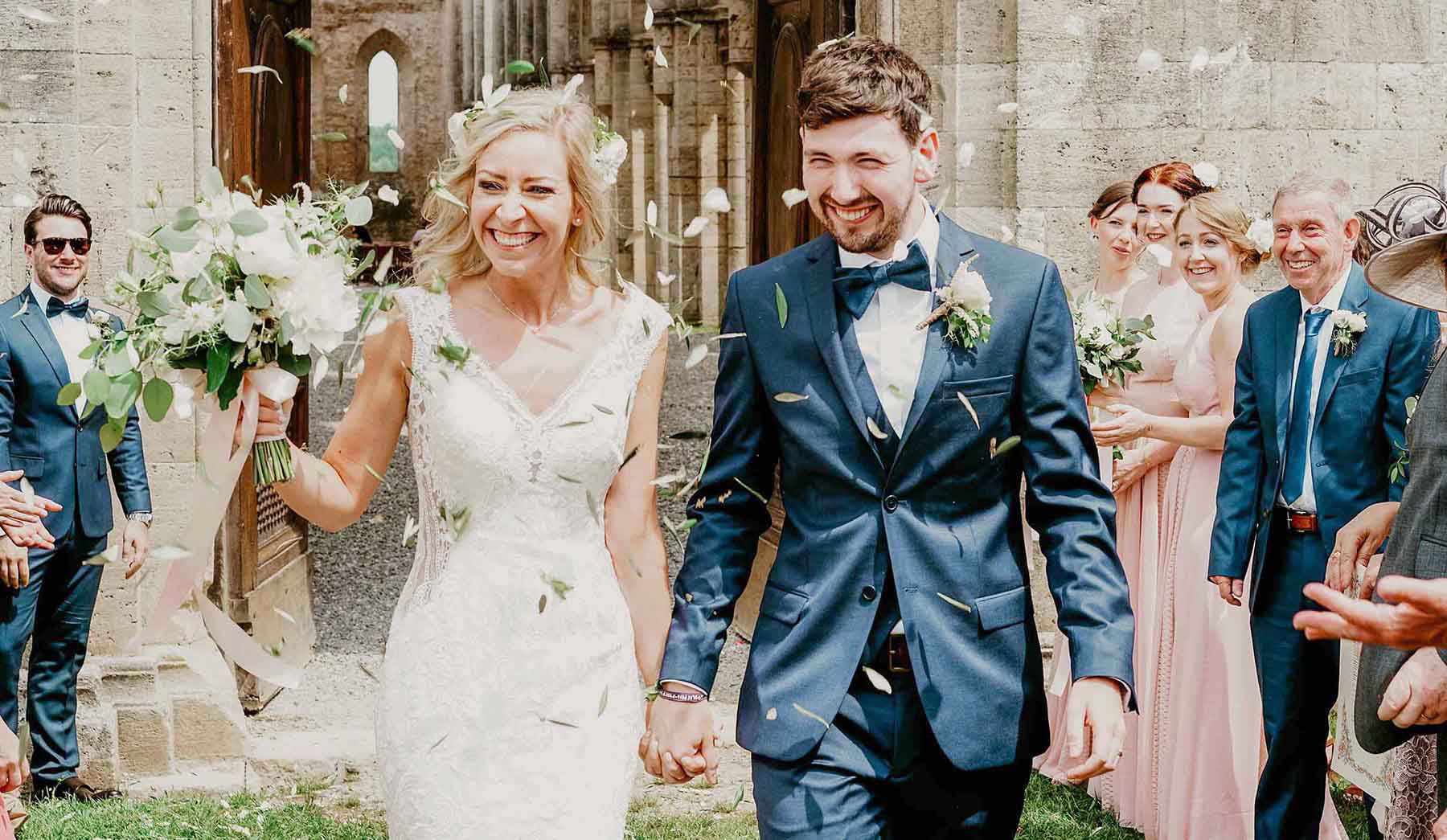 smiling bride and groom in confetti leaving san galgano abbey luxury wedding venue