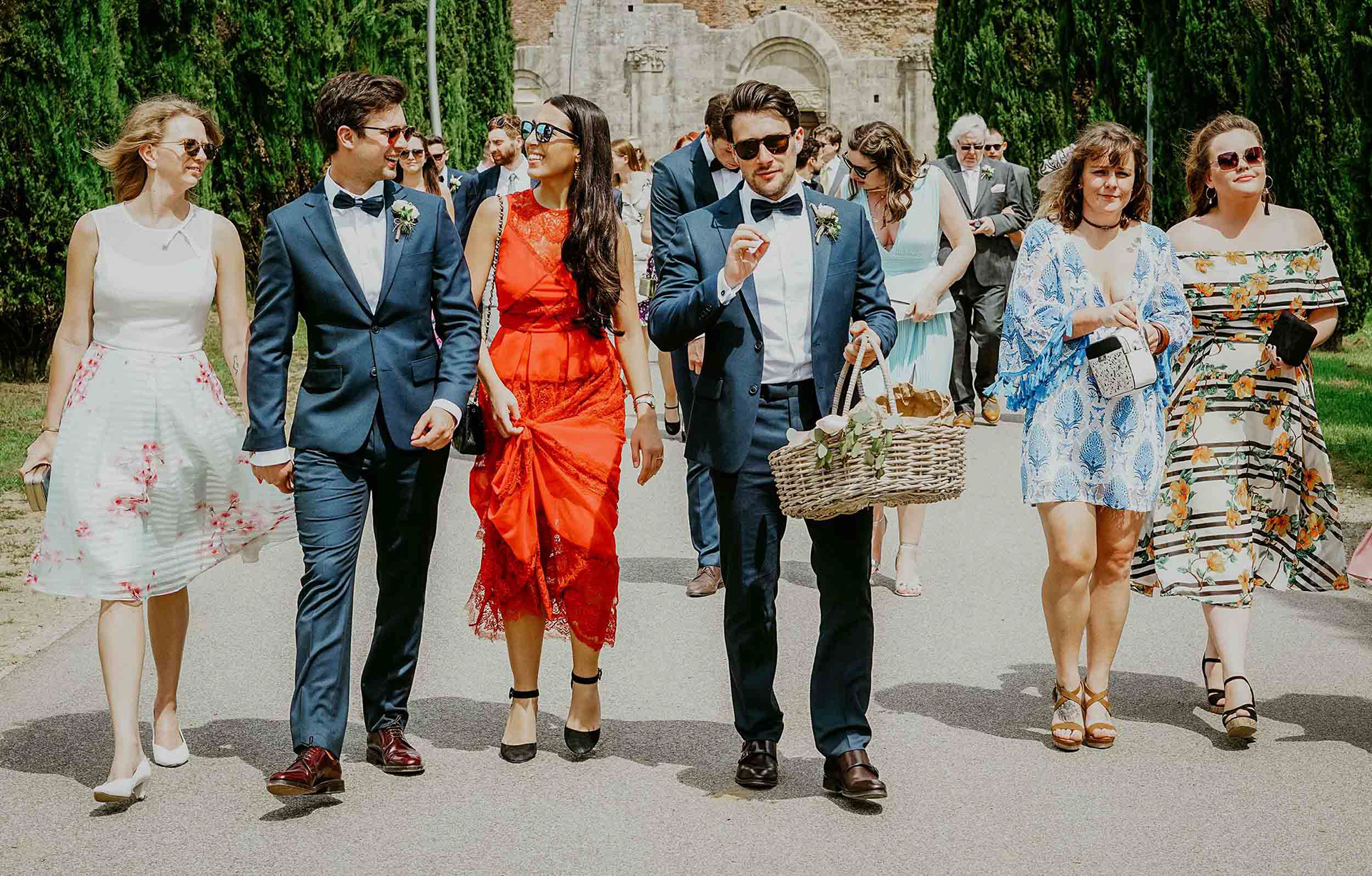 group shot of guests dressed for warm weather walking down italian road at destination wedding in san galgano abbey taken by wedding photographer david lefebvre