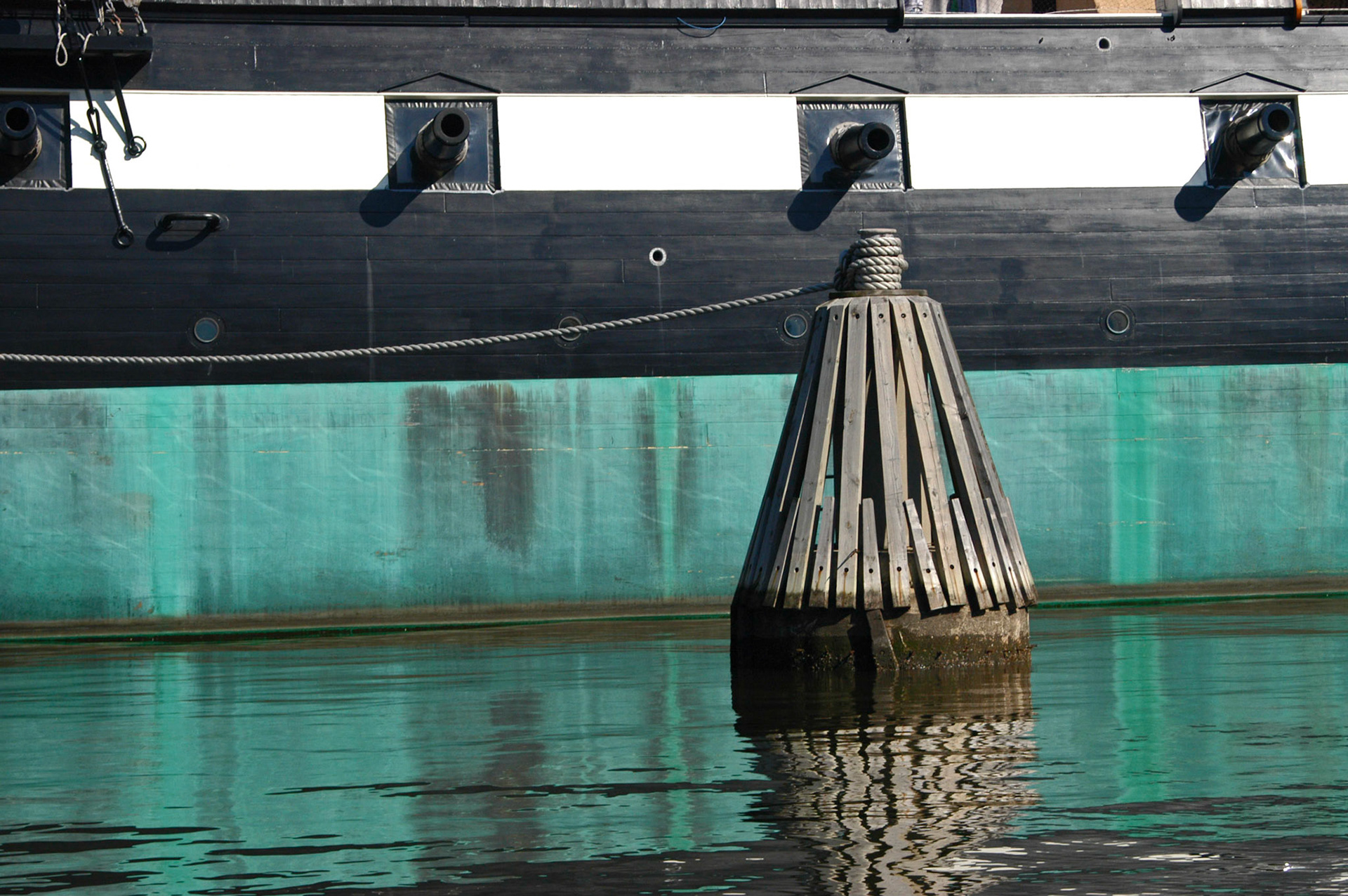 The side of the USS Constellation and a mooring dolphin or piling in Baltimore's inner harbor.
