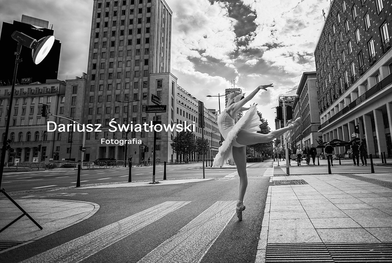 Wydarzenie sesja zdjęciowa na ulicach Warszawy. Organizator Dariusz Światłowski. Na zdjęciu plan z sesji zdjęciowej baletnicy. Tancerka tańczy na przejściu dla pieszych oświetlona światłem studyjnym