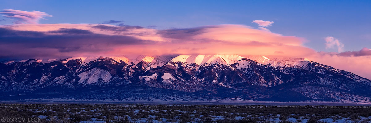 Lenticular clouds cap the snowy Blanca Peak and the Sangre de Cristo Mountains at sunset as they rise above the San Luis Valley in winter, Colorado