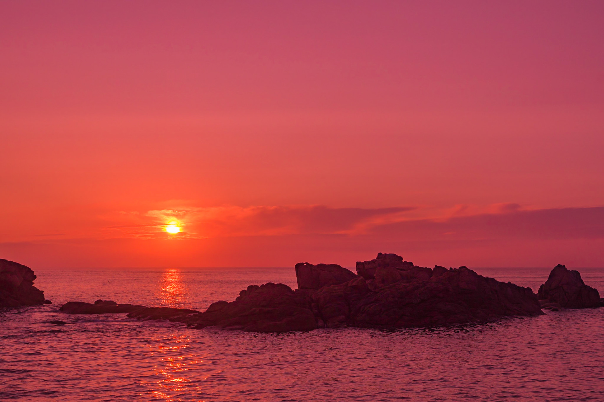 The slightly veiled sun setting over the English Channel at Ploumanach, France, reflecting in the water,  casting a soft dim light over the pink granite rocks.